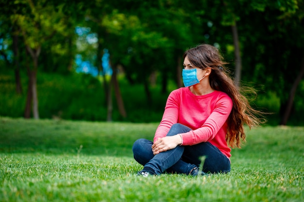 Chica en una máscara médica sobre la naturaleza. Chica descansando en el parque después de la cuarentena COVID-19