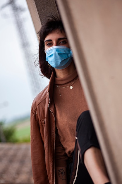 Chica con máscara médica en la ventana de su casa durante el período de cuarentena de covid
