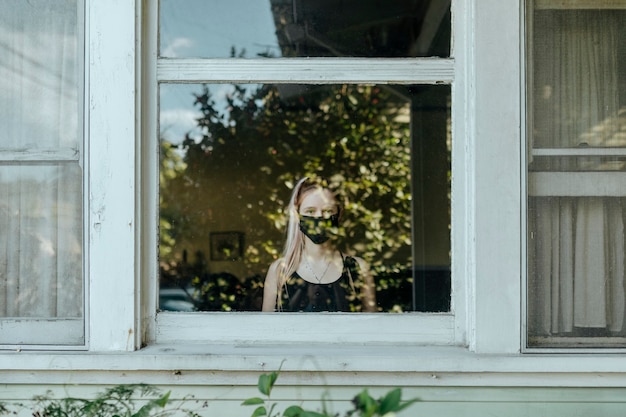 Chica con una máscara mirando por la ventana durante un encierro