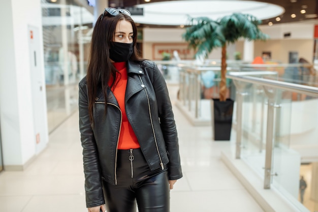 Chica con una máscara negra médica está caminando por un centro comercial. Pandemia de coronavirus. Chica con una máscara protectora está de compras en el centro comercial