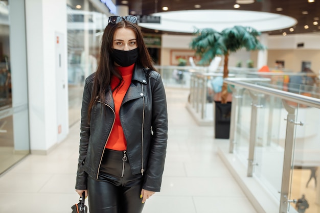 Chica con una máscara negra médica está caminando por un centro comercial. Pandemia de coronavirus.