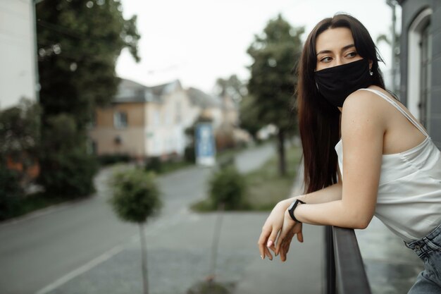 Chica con una máscara protectora en un balcón mira una ciudad vacía.