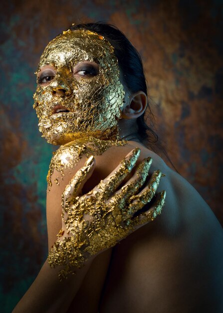 Chica con una máscara en el rostro hecha de pan de oro Retrato de estudio sombrío de una morena