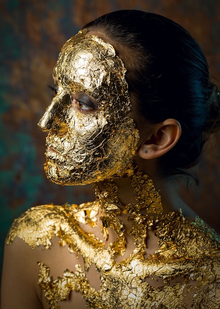 Foto chica con una máscara en el rostro hecha de pan de oro sombrío retrato de estudio de una morena en un resumen