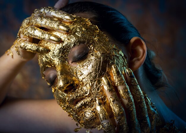 Chica con una máscara en el rostro hecha de pan de oro Sombrío retrato de estudio de una morena