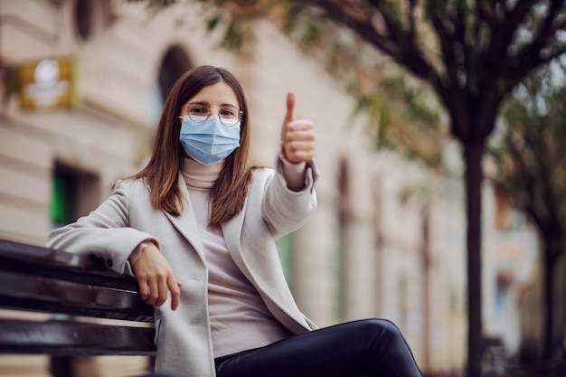 Chica con mascarilla sentada en un banco afuera durante el virus corona