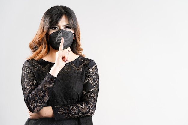 Foto chica con mascarilla con vestido negro sobre fondo blanco.