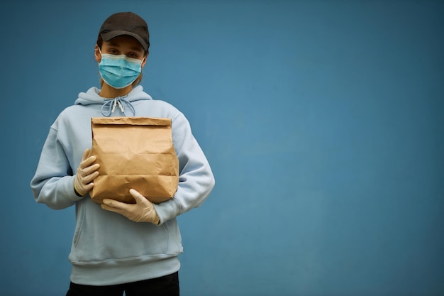 Chica mensajera con una máscara médica y guantes médicos sobre fondo azul.