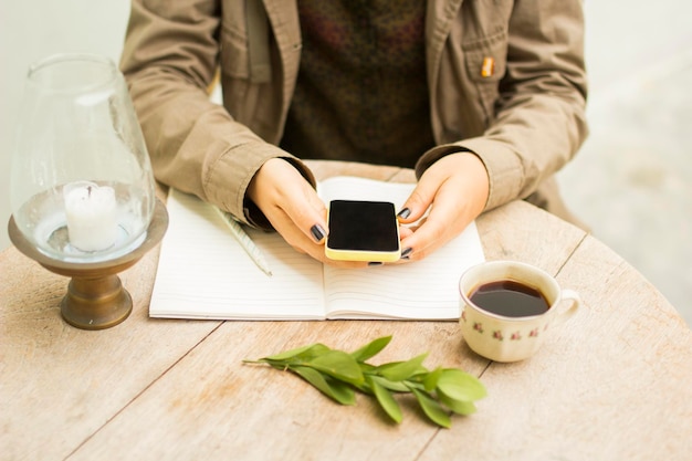 Chica en la mesa con una libreta de celular y una taza de café