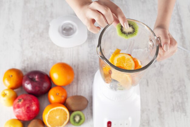 Chica mezclando frutas con batidora eléctrica.