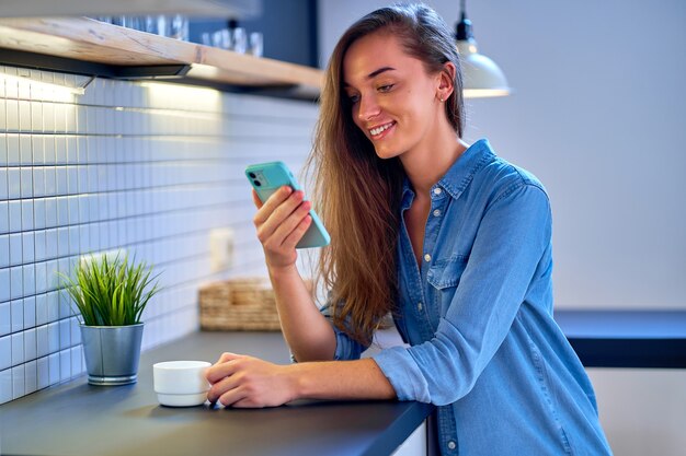 Chica milenaria sonriente feliz casual atractiva joven que usa el teléfono inteligente para la comunicación en línea y ver videos. Gente inteligente con estilo de vida moderno