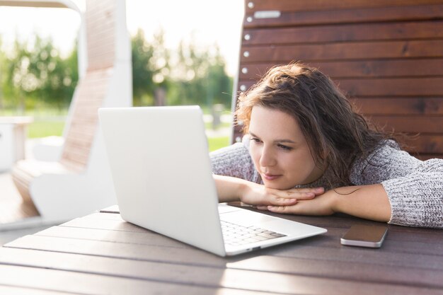 Chica mirando la pantalla del portátil. Mujer joven con teléfono y portátil