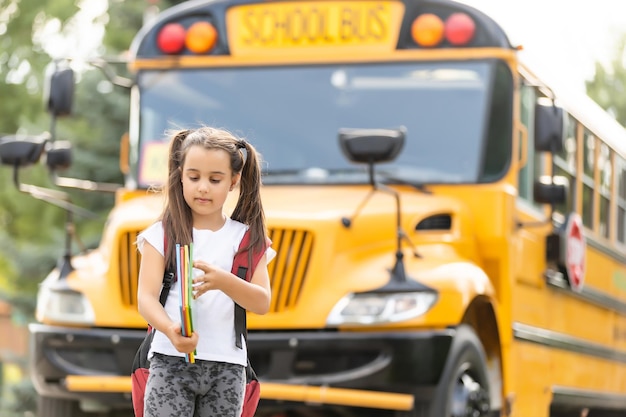 Foto chica con mochila cerca del autobús escolar amarillo. transporte para estudiantes