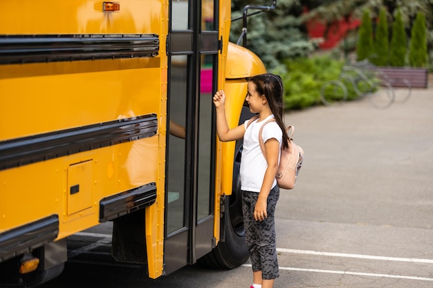 Chica con mochila cerca del autobús escolar amarillo. Transporte para estudiantes