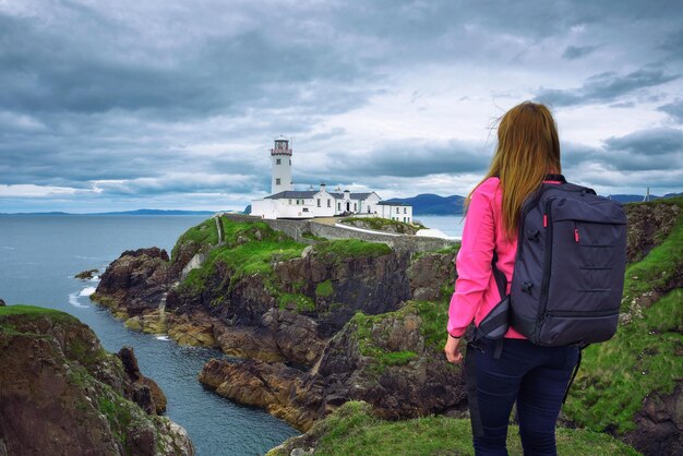 Chica con una mochila mirando el faro de Fanad Head ubicado en la costa norte del condado de Donegal en Irlanda.