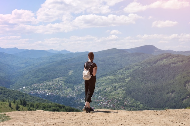 Chica con una mochila de pie en la colina y admirando la vista. Día soleado