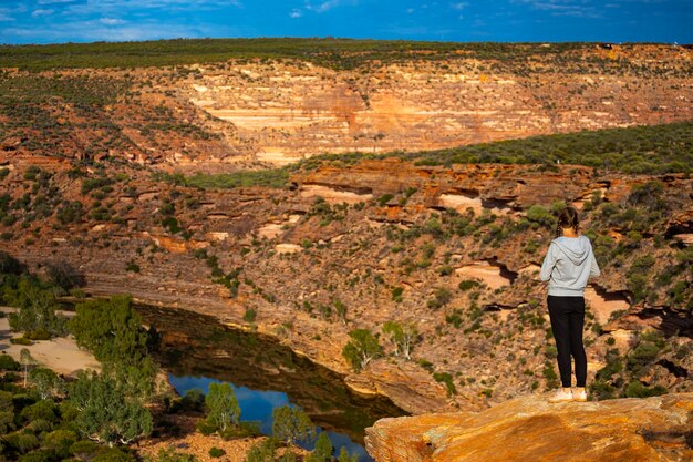 Una chica mochilera se encuentra en la cima de una montaña sobre un río en el Parque Nacional Kalbarri, Australia