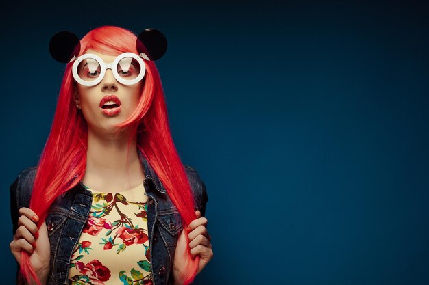 Chica de moda con cabello rosado y grandes gafas de sol sobre fondo azul.