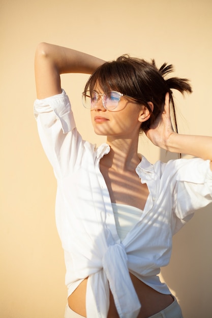 Chica de moda con gafas y una camisa blanca sobre un fondo liso beige con una sombra de una rama