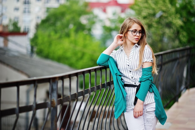 Chica de moda con gafas y jeans rotos contra la barrera en la calle