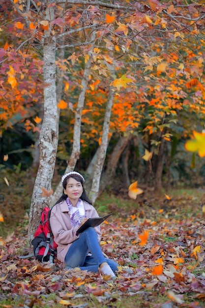 Chica de moda joven con tableta digital sentado en el parque otoño