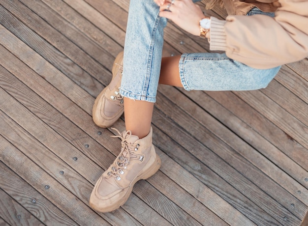 Chica de moda con ropa de invierno de moda en jeans clásicos azules y elegantes zapatos beige de cuero se sienta en un piso de madera vintage