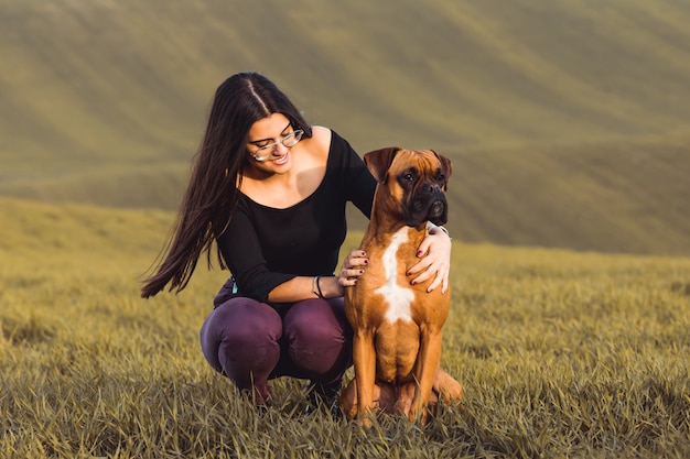 Chica de moda con su perro boxer en el prado en otoño