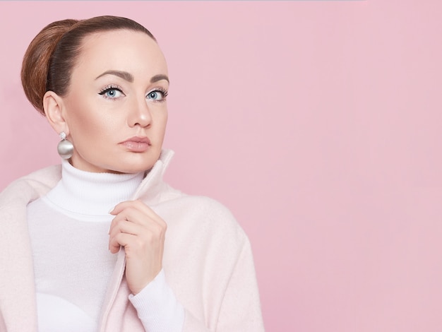 Una chica modelo con un abrigo rosa mira a la cámara y posa