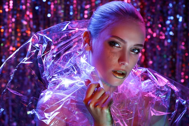 Foto chica modelo de alta moda en coloridas luces de neón brillantes posando en estudio a través de película transparente