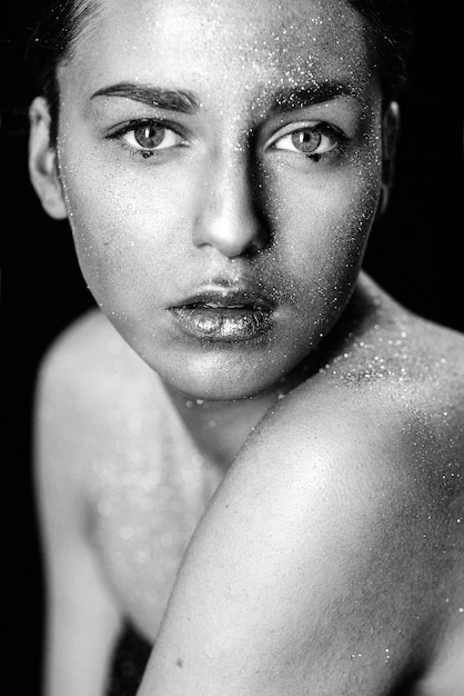 Chica de modelo de arte de moda de belleza con piel dorada. Close Up retrato de niña con ojos azules sobre fondo negro