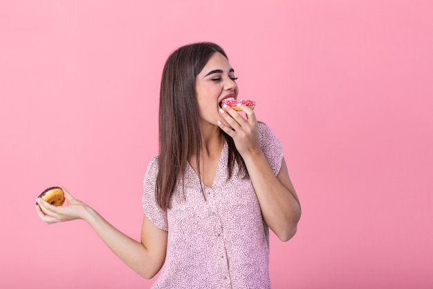 Chica modelo de belleza comiendo donuts coloridos. Mujer de estilo alegre divertido elegir dulces sobre fondo rosa.