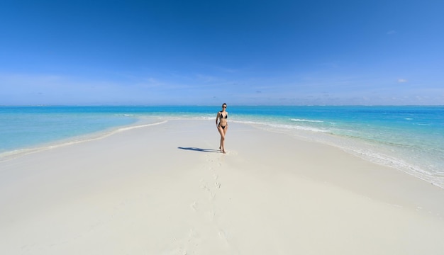 chica modelo en bikini negro en la arena blanca junto al océano