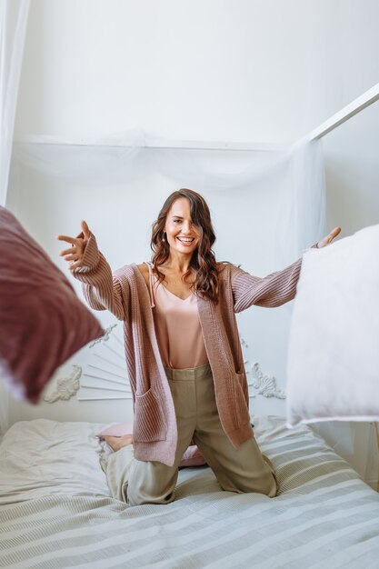 Chica modelo en una chaqueta de punto estirada en la cama. Tirar almohadas hacia adelante