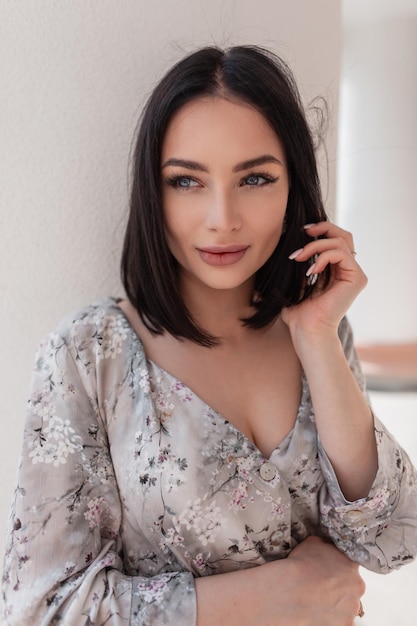 Chica modelo hermosa y elegante con piel natural clara y ojos azules en un vestido floral de moda se encuentra cerca de la pared blanca en la ciudad Estilo de ropa de mujer de verano