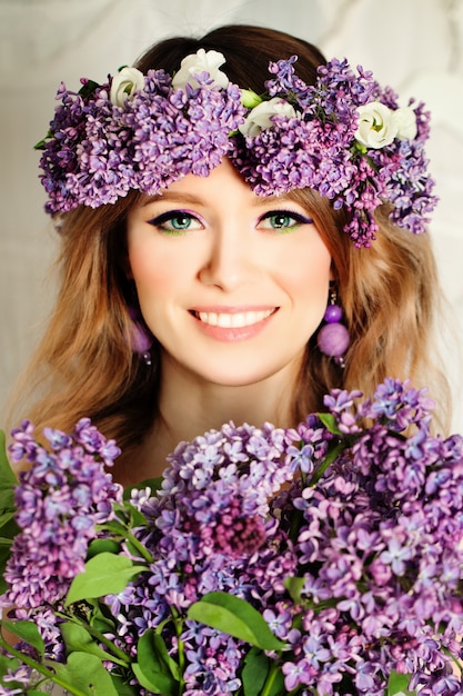 Chica modelo de moda de belleza con estilo de pelo de flores de color lila. Mujer hermosa y flores florecientes. Peinado de la naturaleza. Maquillaje y accesorios creativos de color violeta navideños
