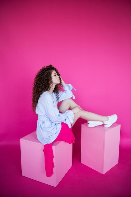 Chica modelo de moda con cabello sano brillante ondulado rizado sobre fondo rosa Cuidado del cabello maquillaje brillante