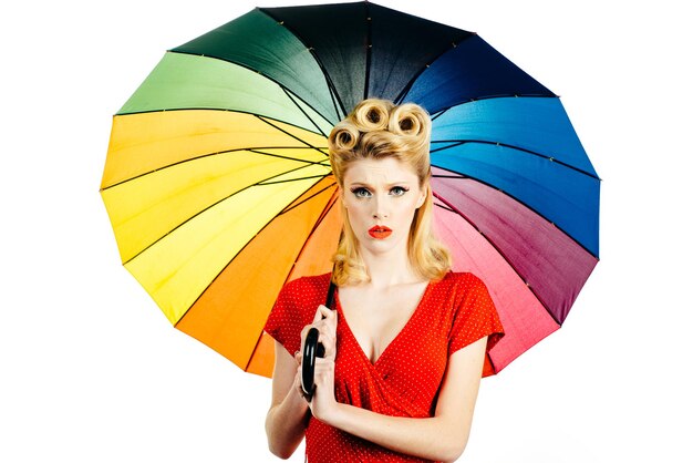 Chica modelo con paraguas de arco iris en tiempo de lluvia. Estado de ánimo de otoño lluvioso, pin up mujer vestido rojo aislado blanco.