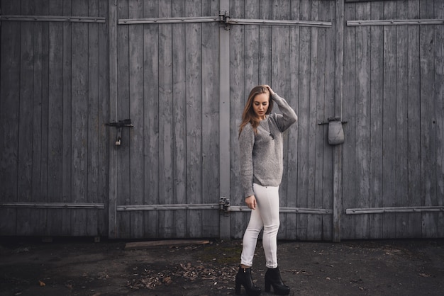 Chica modelo rubia con pantalón blanco, suéter gris y botas negras