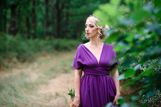 Chica modelo rubia con un vestido lila con un ramo con un bosque verde