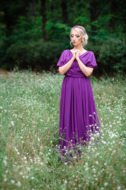 Foto chica modelo rubia con un vestido lila con un ramo con un bosque verde