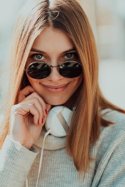 una chica moderna con gafas de sol caminando por la calle escucha música con auriculares.