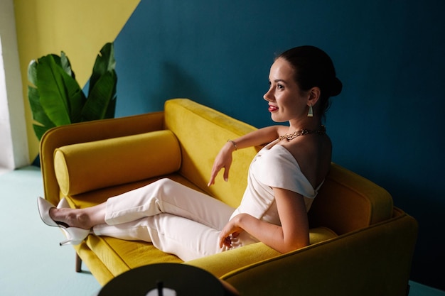 Una chica con un mono blanco se sienta en un sofá amarillo.