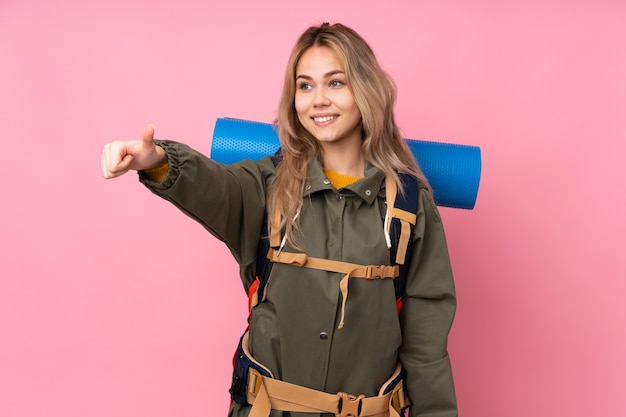 Chica montañista adolescente con una mochila grande aislada en rosa dando un pulgar hacia arriba gesto