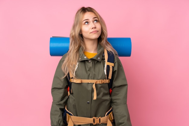 Chica montañista adolescente con una mochila grande aislada en rosa y mirando hacia arriba