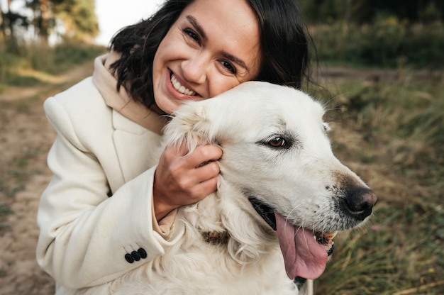 Chica morena abrazando golden retriever blanco en el campo