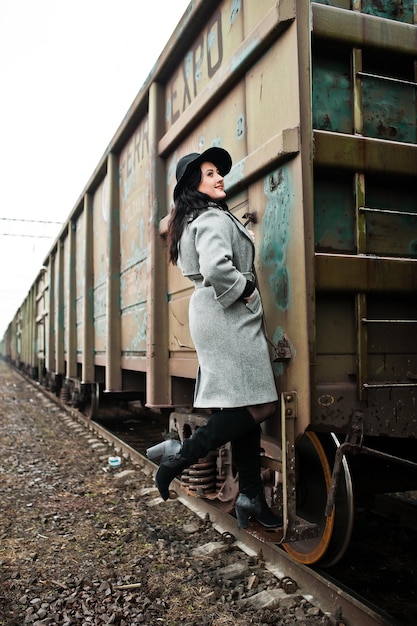 Chica morena con abrigo gris con sombrero en la estación de tren