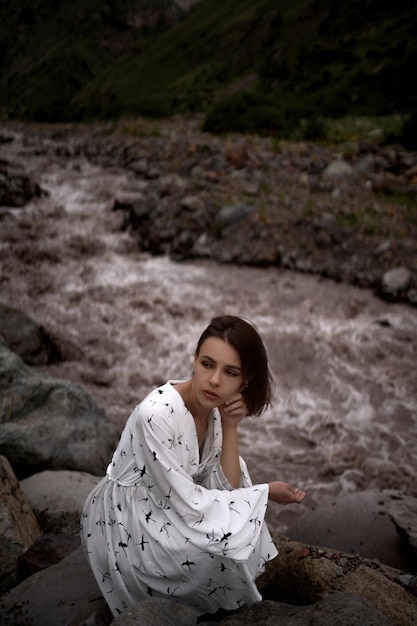 Chica morena atractiva está sentada al lado del río y mirando hacia otro lado