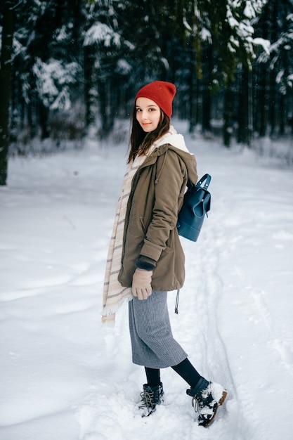 Chica morena atractiva joven con una bufanda caliente y un sombrero rojo posando en el bosque de nieve