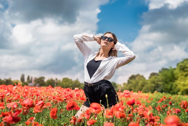 Chica morena en blusa blanca caminando por un campo de amapolas