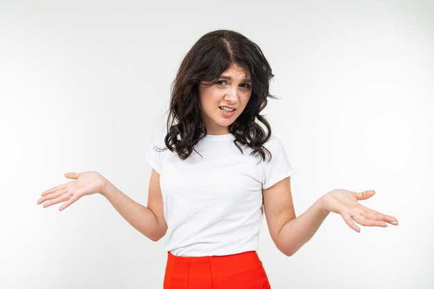 Chica morena en una camiseta blanca dudas sobre un fondo blanco de estudio